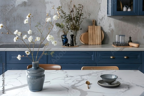 Empty and clean marble dining table in scandinavian kitchen. Modern monochrome interior with blue drawers on wooden furniture. Tablewear and vases with flowers - generative ai photo