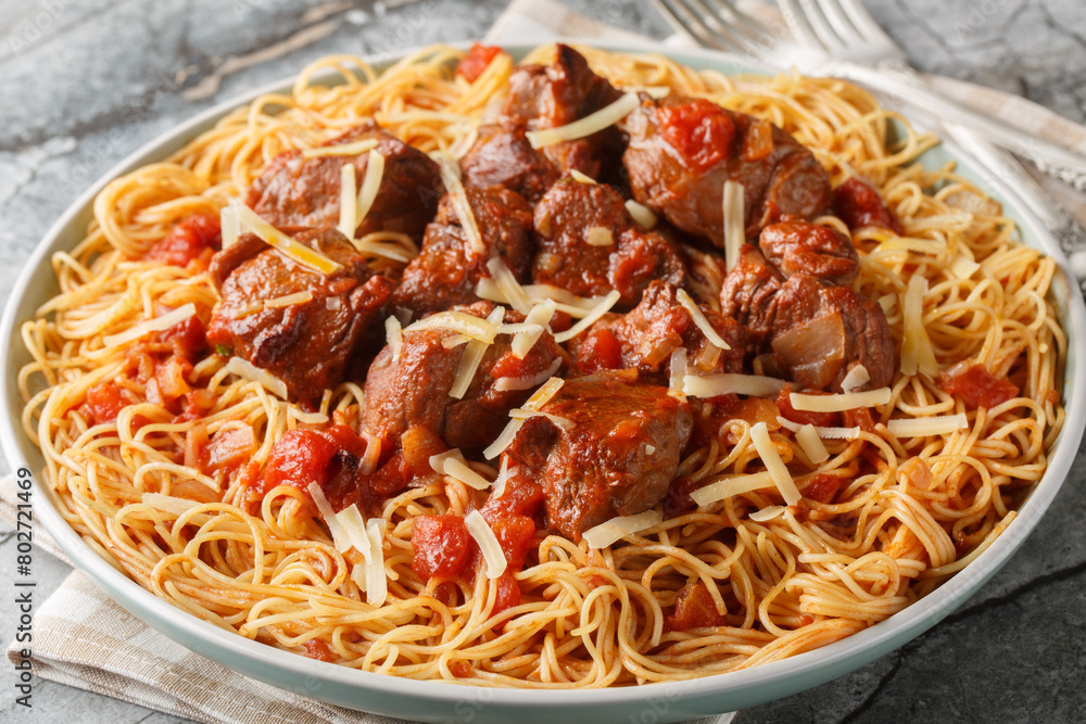 Moshari Kokkinisto or Tas Kebap Greek Veal Stew in a Tomato Sauce with pasta spaghetti closeup on the plate on the table. Horizontal Moshari Kokkinisto or Tas Kebap Greek Veal Stew in a Tomato Sauce with pasta spaghetti closeup on the plate on the table. Horizontal
