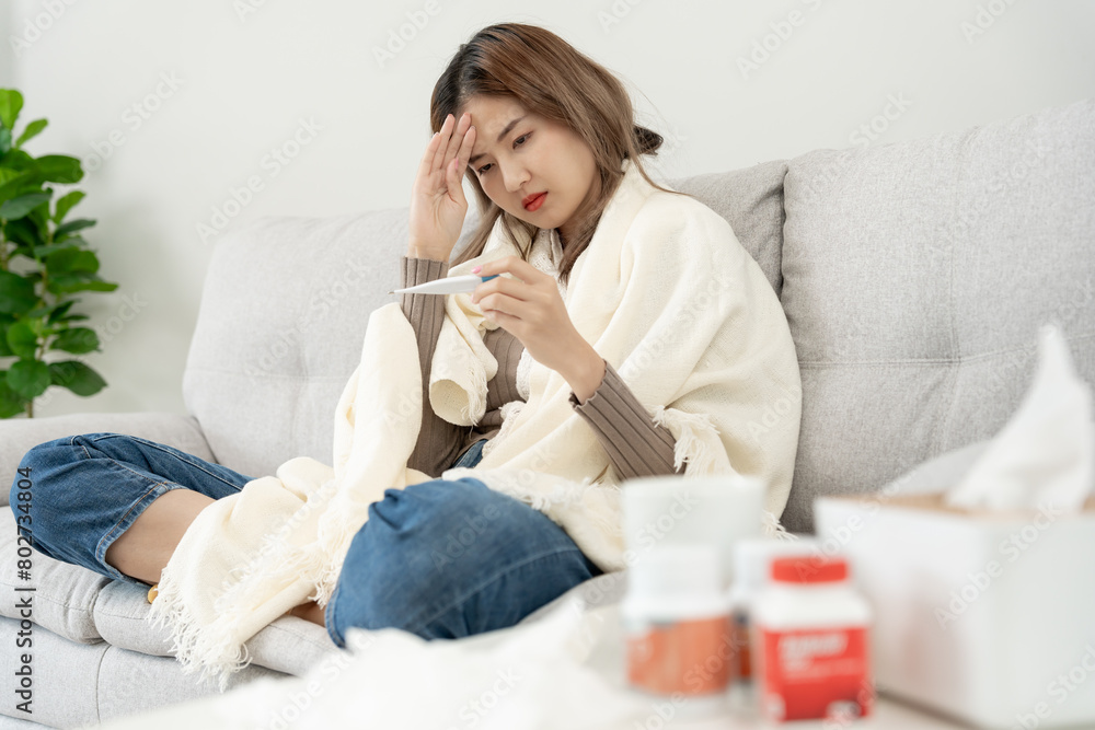 Young Asian woman having high fever while checking body temperature, female sneezing and runny nose with seasonal influenza, allergic, digital thermometer, virus, coronavirus, illness, respiratory Young Asian woman having high fever while checking body temperature, female sneezing and runny nose with seasonal influenza, allergic, digital thermometer, virus, coronavirus, illness, respiratory