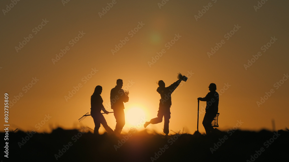A group of cheerful farmers dancing in a field at sunset