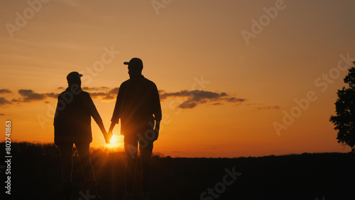 Holding hands, a couple watches the sunset over the grassy field.