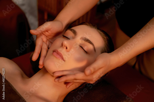 Caucasian woman enjoying relaxing anti-stress head massage and pampering facial beauty skin recreation leisure in warm candle lighting ambient salon spa in luxury resort or hotel. Quiescent