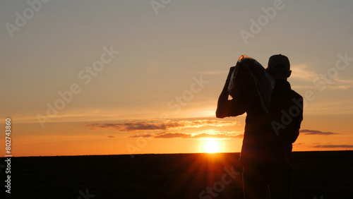 Silhouette of a farmer with a bag on his shoulder standing in a field at sunset. Back view