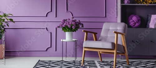 Actual image of a grey wooden armchair placed on a patterned black and white rug in an artistic living room setting featuring a geometric violet wall and cabinet. photo