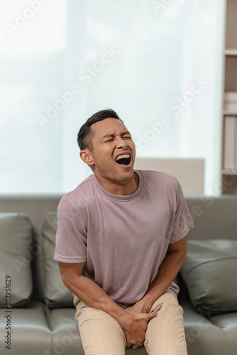 A man is sitting on a sofa and touching his crotch. The concept of holding back pee, missing the bathroom, prostate cancer, UTI or urinary tract infection.