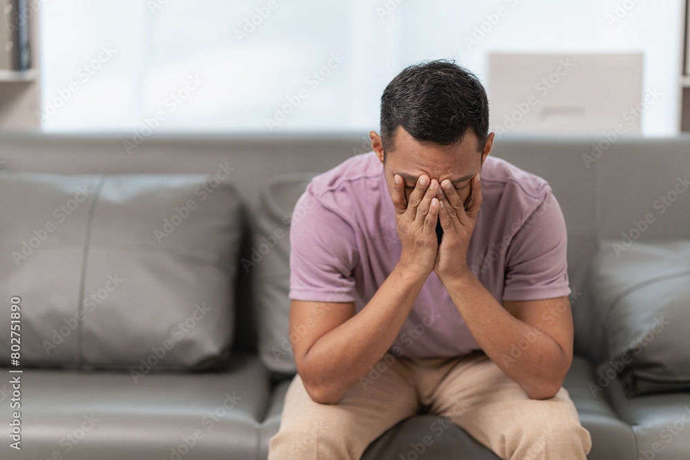 Sad man suffering from a headache or migraine touching his temples who is massaging his head, stressed sitting on the sofa with a pained expression on his face. Feeling weak or depressed Sad man suffering from a headache or migraine touching his temples who is massaging his head, stressed sitting on the sofa with a pained expression on his face. Feeling weak or depressed