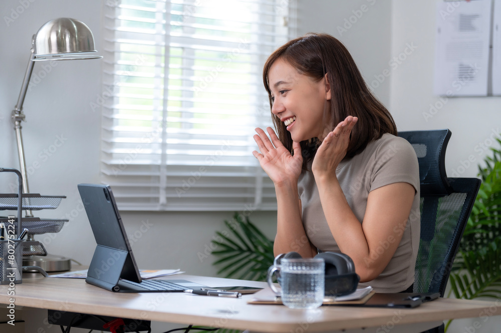 A woman is sitting at a desk with a laptop and a cup of water. She is smiling and she is happy A woman is sitting at a desk with a laptop and a cup of water. She is smiling and she is happy