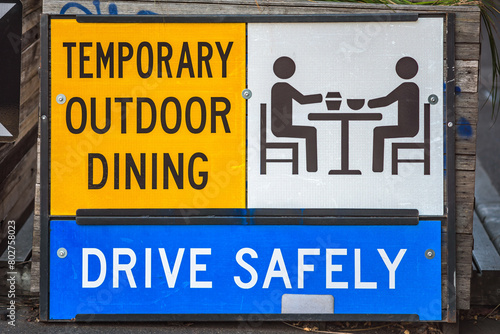 A road sign instructing drivers to 'DRIVE SAFELY' due to the presence of 'TEMPORARY OUTDOOR DINING'