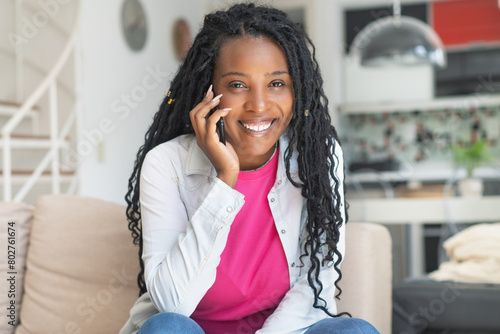 Pretty african american woman with dreadlocks talking at phone indoors at living room