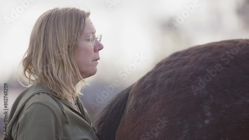 Tears run down woman's cheek standing behind horse during equine therapy, profile photo