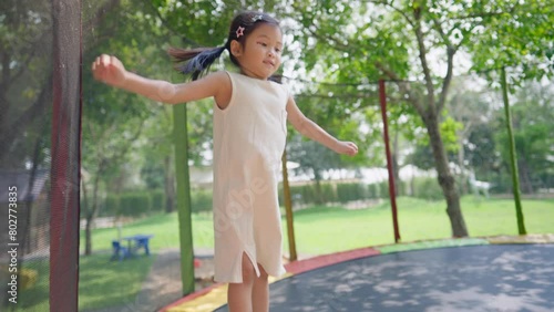 Active asian girl jumping on the tempoline outdoor park on the sunny day, showing healthy and happy activities outside the house, kids leisure, learning by playing, child muscles and bones development