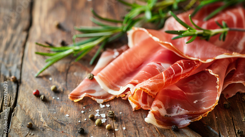 Sliced prosciutto with rosemary on wooden table