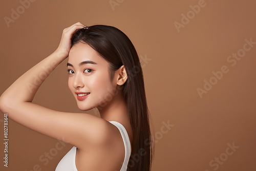 A beautiful Asian woman with smooth skin posing in a white tank top on a brown background, touching her hair with her back view, smiling and looking at the camera in the style of copy space concept