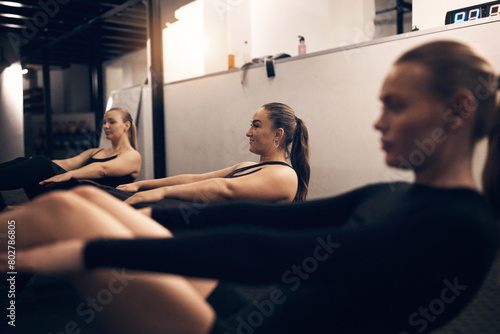 Focused group of fit young women in sportswear doing core exercises together on the floor of a gym during a workout class photo