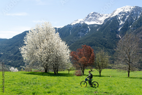 Male biker in a green meadow surrounded of snowcapped mountains on a sunny spring day.