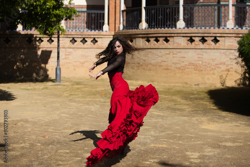 Beautiful woman dancing flamenco in Seville, Spain. She wears a red and black dress typical of a flamenco dancer with a lot of art, you can see the movement in the air of the frilly dress.