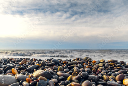 Coastal pebbles. Pebbles on the seashore in close-up. A rocky beach. Stones in close-up with a bokeh effect. Grey natural background. Wet pebbles imprinted on the sand on a sunny day. Selective focus.