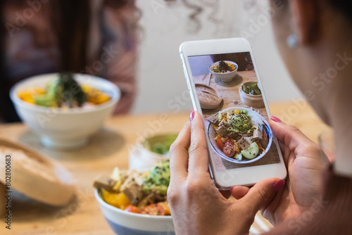 Two girlfriends having healthy lunch in cafe. Young woman taking picture of food with smartphone posting on social media photo