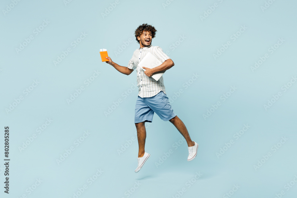 Full body traveler man wear casual clothes hold passport ticket laptop pc computer jump high isolated on plain blue background. Tourist travel abroad in free time rest getaway Air flight trip concept Full body traveler man wear casual clothes hold passport ticket laptop pc computer jump high isolated on plain blue background. Tourist travel abroad in free time rest getaway Air flight trip concept