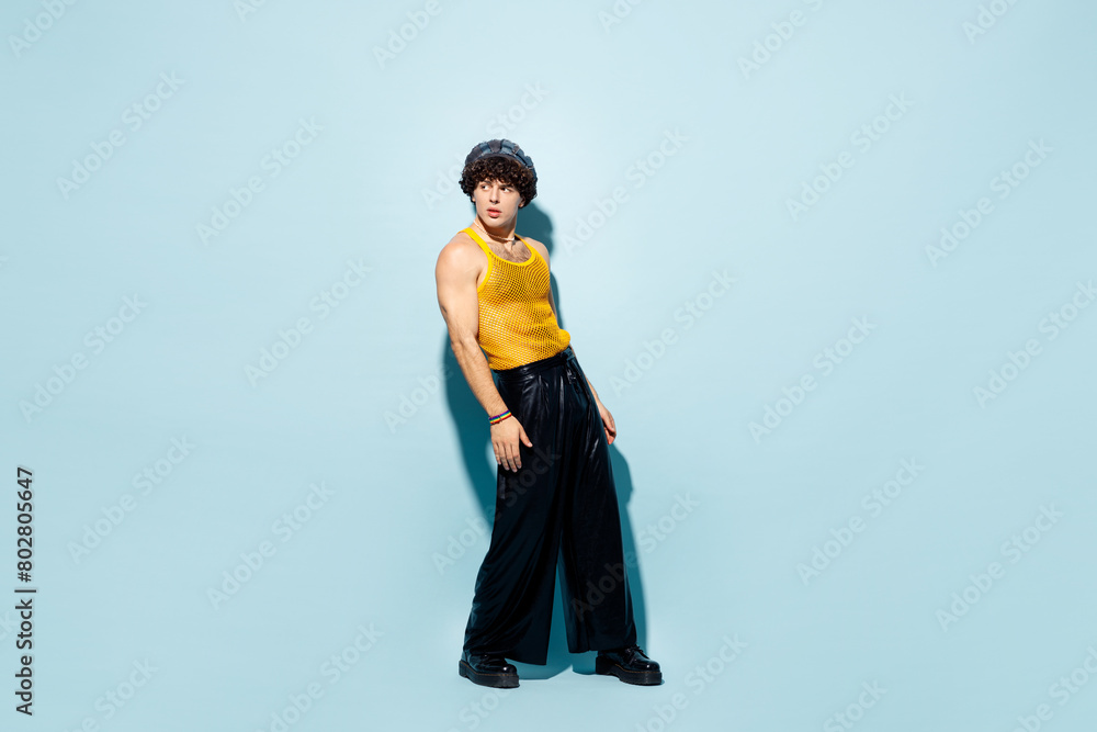 Full body side view young happy gay Latin man he wear mesh tank top hat clothes look aside isolated on plain pastel light blue cyan background studio portrait. Pride day June month love LGBT concept.