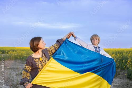 portrait of a Ukrainian family  mother and son with a blue-yellow flag against the backdrop of a blooming rapeseed field. Ukraine s Independence Day. support Ukraine. Stop the war