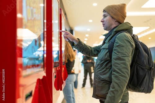 Man interacts with digital kiosk in modern mall, navigating touch screen. Technological integration into shopping experiences.