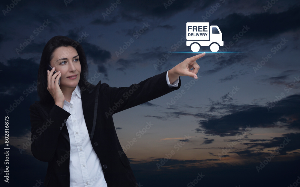 Businesswoman talking on her cell phone and pointing finger to free delivery truck icon over sunset sky, Business transportation service concept Businesswoman talking on her cell phone and pointing finger to free delivery truck icon over sunset sky, Business transportation service concept