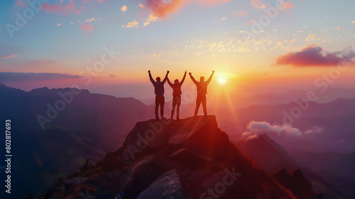 Three people standing at the top of a mountain with arms raised celebrating success, with dramatic lighting, in a drone view capturing a panoramic photo of the mountain landscape