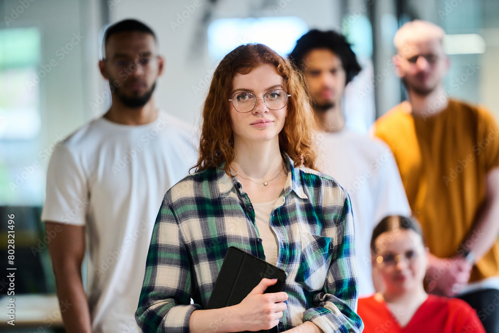 Fototapeta premium A diverse group of young business people walking a corridor in the glass-enclosed office of a modern startup, including a person in a wheelchair and a woman wearing a hijab