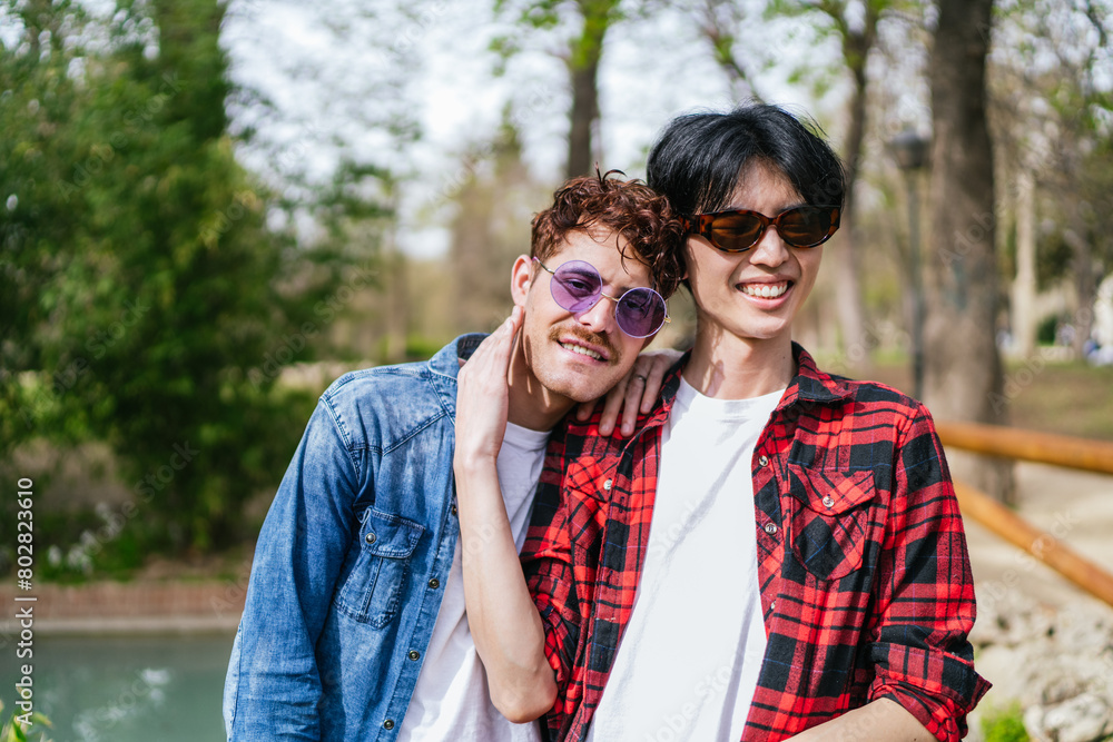Fototapeta premium Cheerful Chinese man in an LGBT relationship hugs his partner, both smiling in a park.