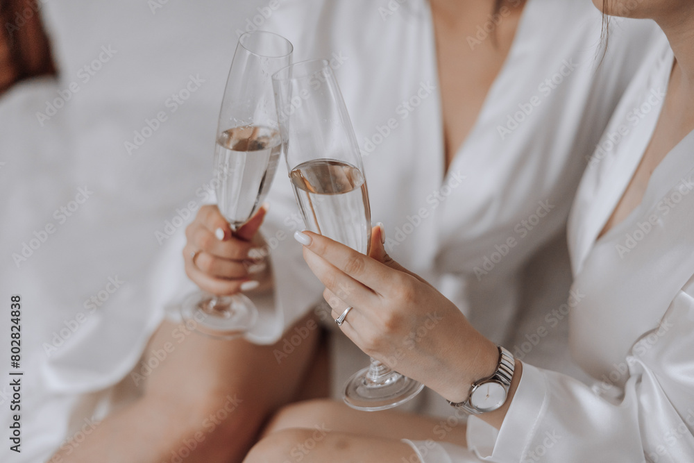 Two women are sitting on a bed, holding glasses of champagne and smiling. Scene is celebratory and happy Two women are sitting on a bed, holding glasses of champagne and smiling. Scene is celebratory and happy
