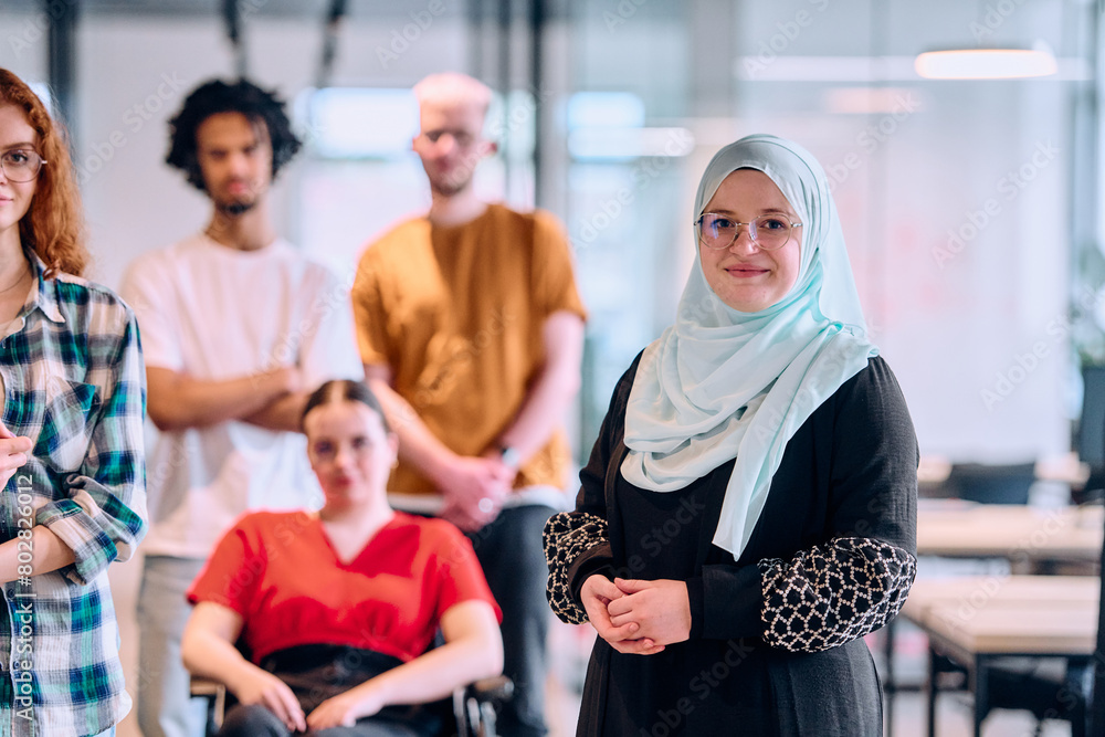 Obraz premium A diverse group of young business people walking a corridor in the glass-enclosed office of a modern startup, including a person in a wheelchair and a woman wearing a hijab
