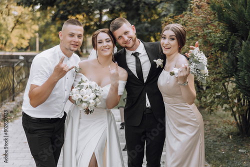 A bride and groom are posing for a photo with their friends. The bride is wearing a white dress and the groom is wearing a black suit. The friends are standing behind them