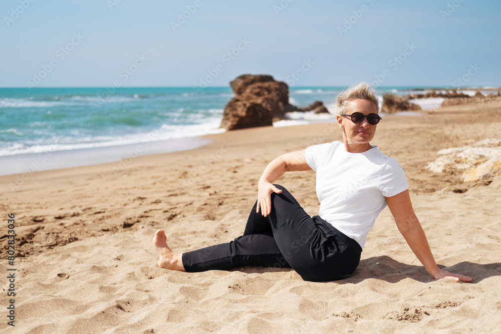 Middle Aged Female Doing Spinal Twist Yoga Exercises. Mindfulness Zen Spiritual Meditation Tips. Kundalini Yoga. Reiki Meditation. Relaxing. Unity With Nature. Sea or Ocean Coast Beach Middle Aged Female Doing Spinal Twist Yoga Exercises. Mindfulness Zen Spiritual Meditation Tips. Kundalini Yoga. Reiki Meditation. Relaxing. Unity With Nature. Sea or Ocean Coast Beach