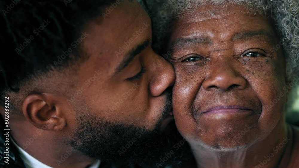 Adult grandson kissing elderly African American grandmother on the cheek in loving affectionate moment between two intergenerational family members Adult grandson kissing elderly African American grandmother on the cheek in loving affectionate moment between two intergenerational family members