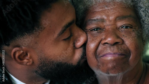 Adult grandson kissing elderly African American grandmother on the cheek in loving affectionate moment between two intergenerational family members photo