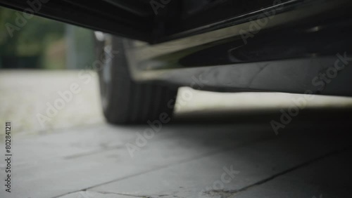 Close-up of a car's side and undercarriage on a paved surface, person leaving on high heels, shallow focus. photo