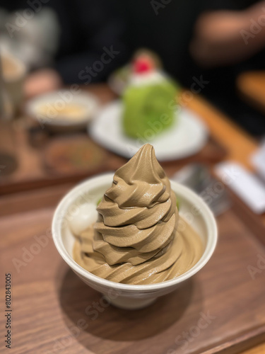 A Japanese milk chocolate soft serve ice cream in a bowl in the foreground and a slice of green tea cake in the background