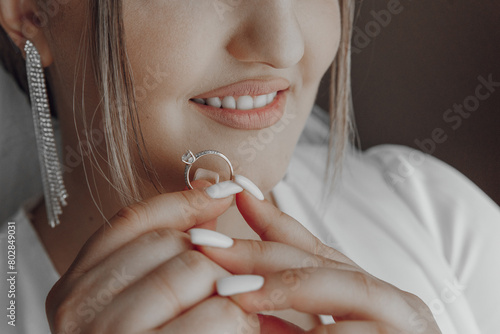 A woman is holding a ring in her hand, and she is smiling. The ring is a diamond ring, and it is a beautiful piece of jewelry. The woman's smile suggests that she is happy and proud of the ring