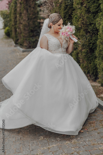 A woman in a white wedding dress is walking down a street holding a bouquet of pink flowers