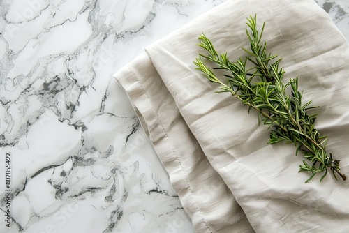 Folded linen napkin with green plant on marble table background top view