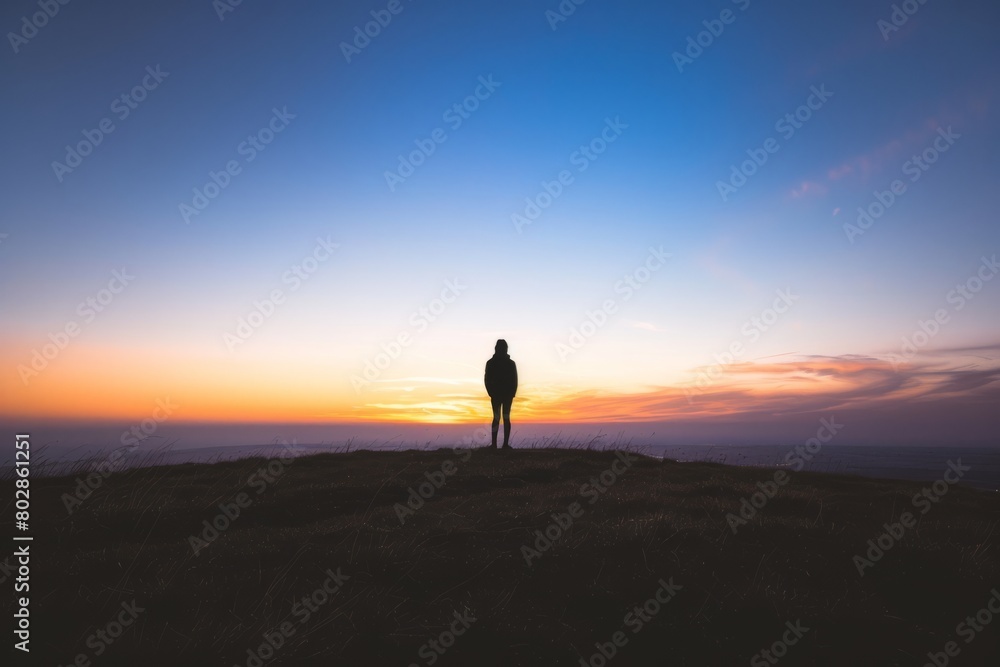 Step into the serene silhouette of a lone figure standing on a hilltop, watching as the sun sinks below the horizon and casts long, Generative AI