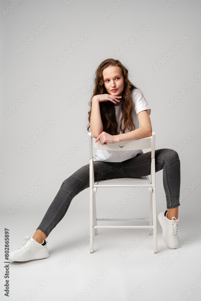 Fototapeta premium Curly girl model posing on a chair against gray background