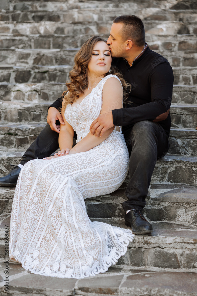 A man and woman are sitting on a set of stairs, the woman is wearing a white dress A man and woman are sitting on a set of stairs, the woman is wearing a white dress