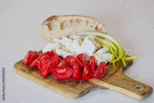 Cheese, tomatoes, green onions and bread on a wooden plate.