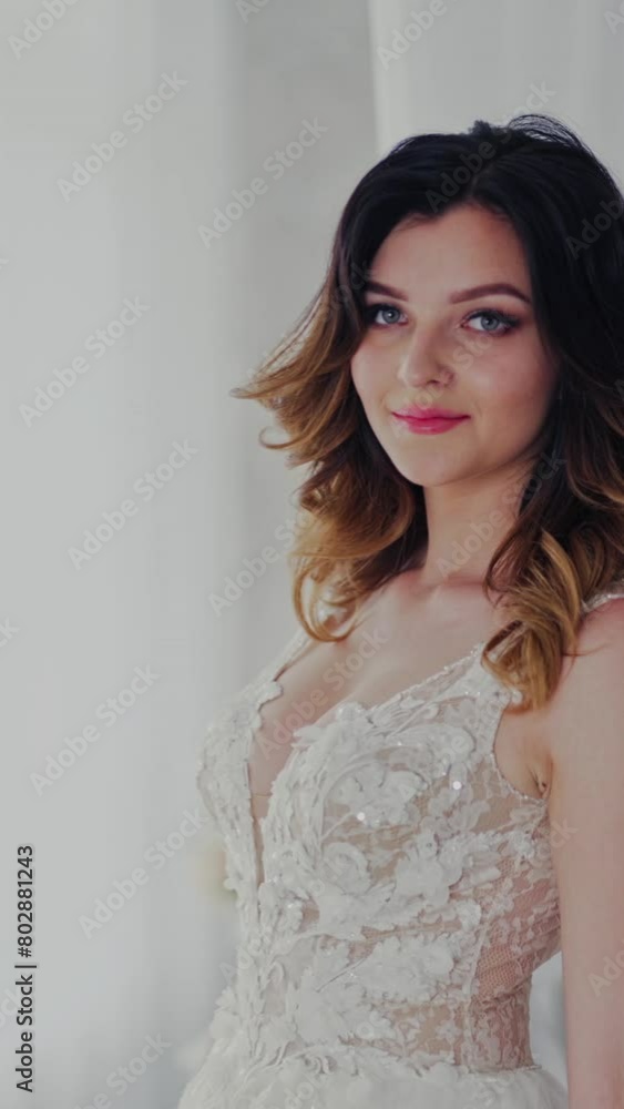 Sexy wedding lace dress on a beautiful model in the light studio. Attractive bride in luxurious dress with bouquet of flowers is coming to the window in bedroom. Vertical video Sexy wedding lace dress on a beautiful model in the light studio. Attractive bride in luxurious dress with bouquet of flowers is coming to the window in bedroom. Vertical video