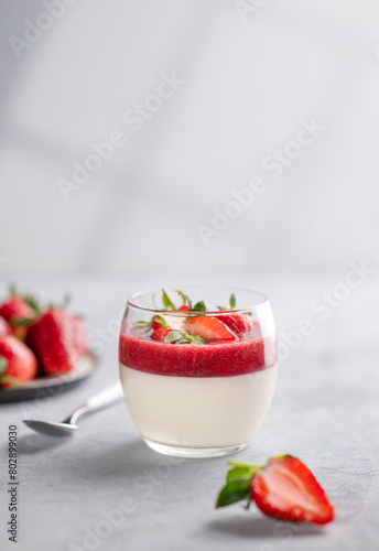 Panna cotta with strawberry and cream in glass with fresh berries on a light background close up with shadow.