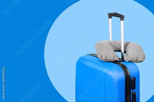 Blue suitcase and travel pillow on a blue background.