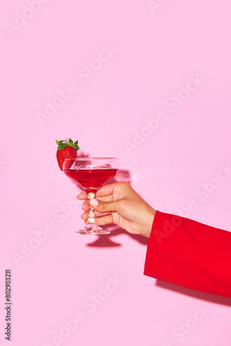 Female hand holding sweet cocktail with strawberry and coconut against pink background. Relaxation. Concept of alcohol and non-alcohol drink, party, holidays, bar, mix. Poster. Copy space for ad