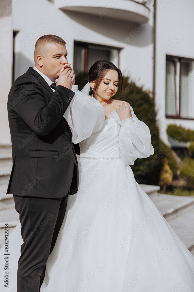 A bride and groom are standing on a staircase, the bride is wearing a white dress and the groom is wearing a black suit